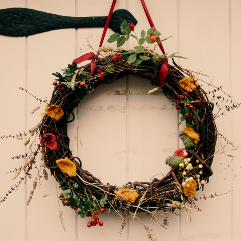 A natural autumn wreath with berries, leaves, knitted leaves and acorns, on a white cottage front door.