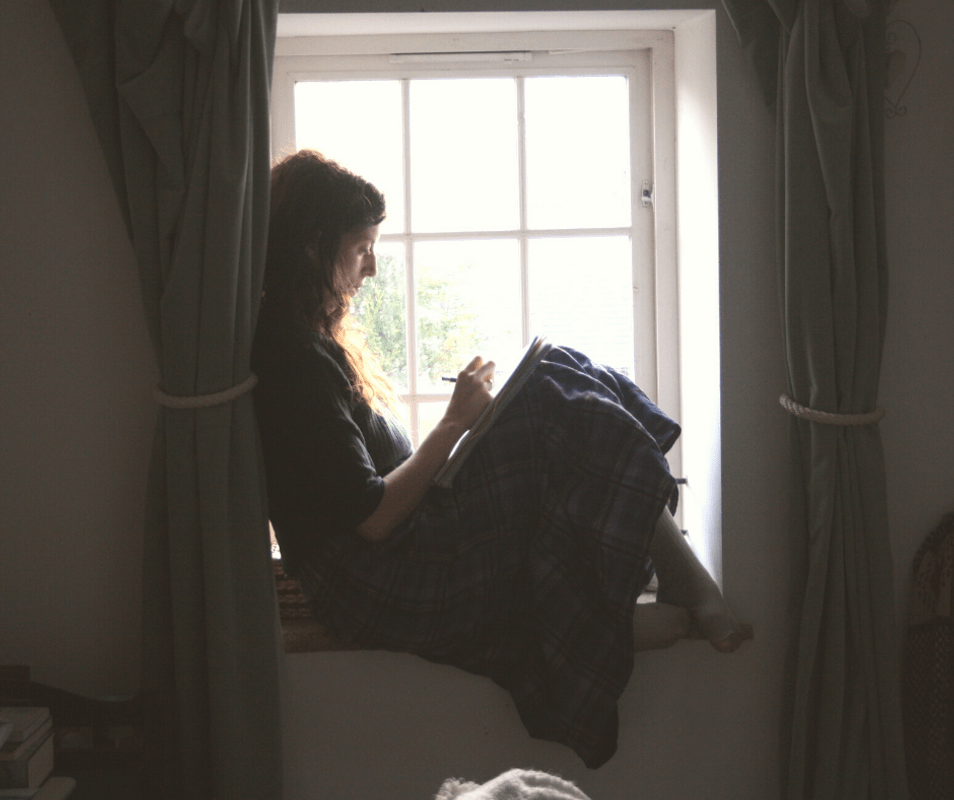 woman sitting on window sill writing a pregnancy to do list